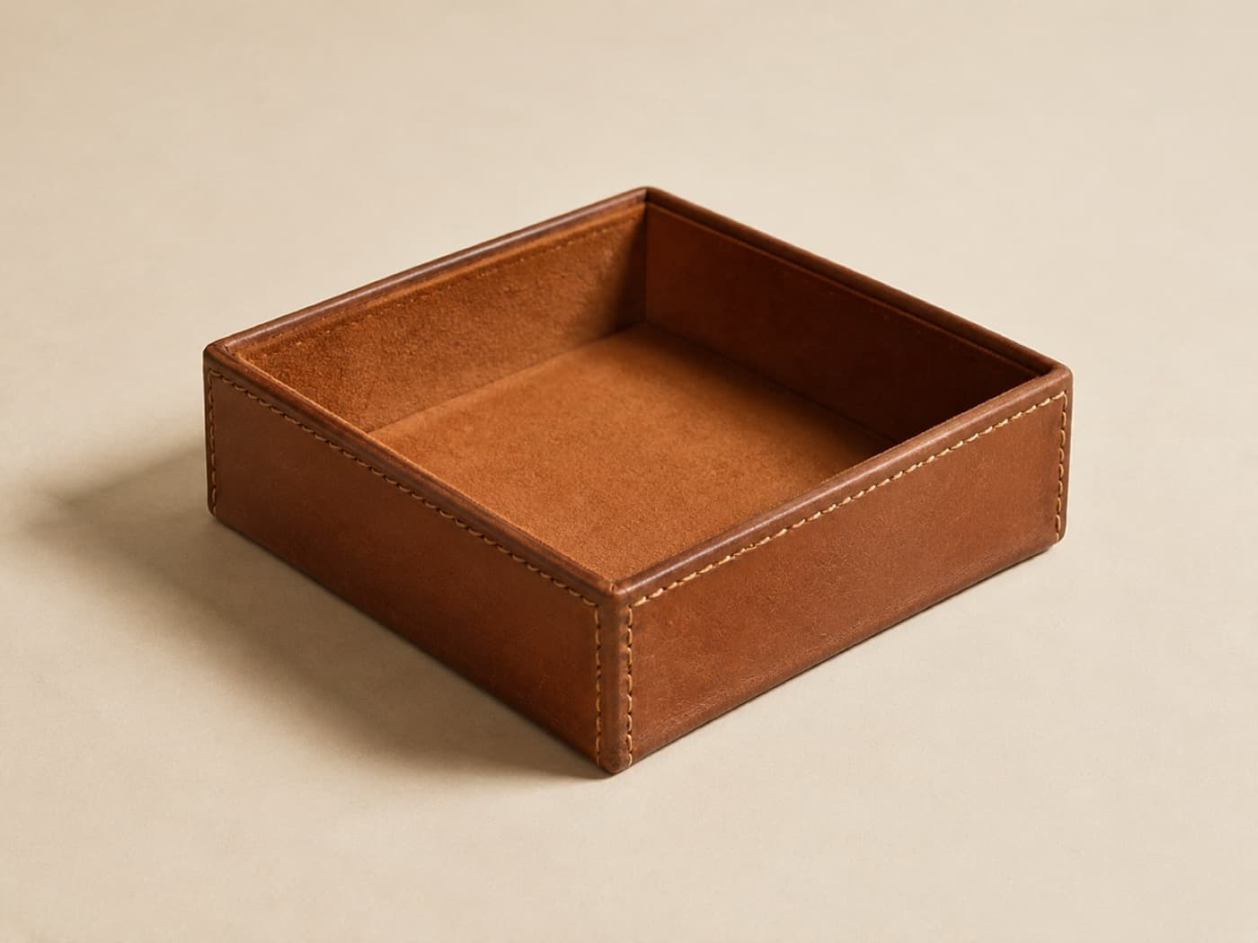 A deep square leather box with stitched corners, photographed at an angle
