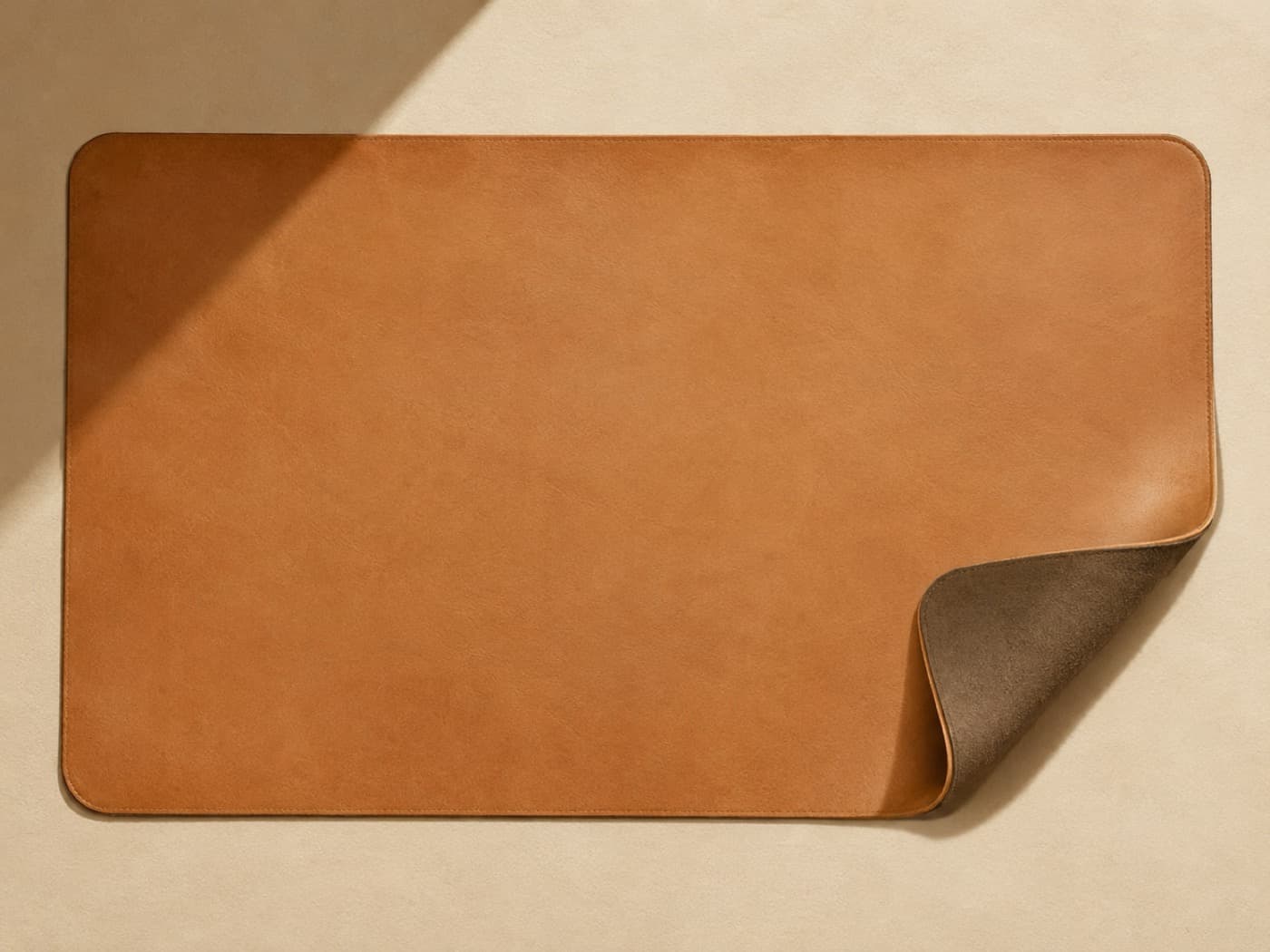 An extra-large leather desk mat seen from above with one corner rolled back to show the felt underside