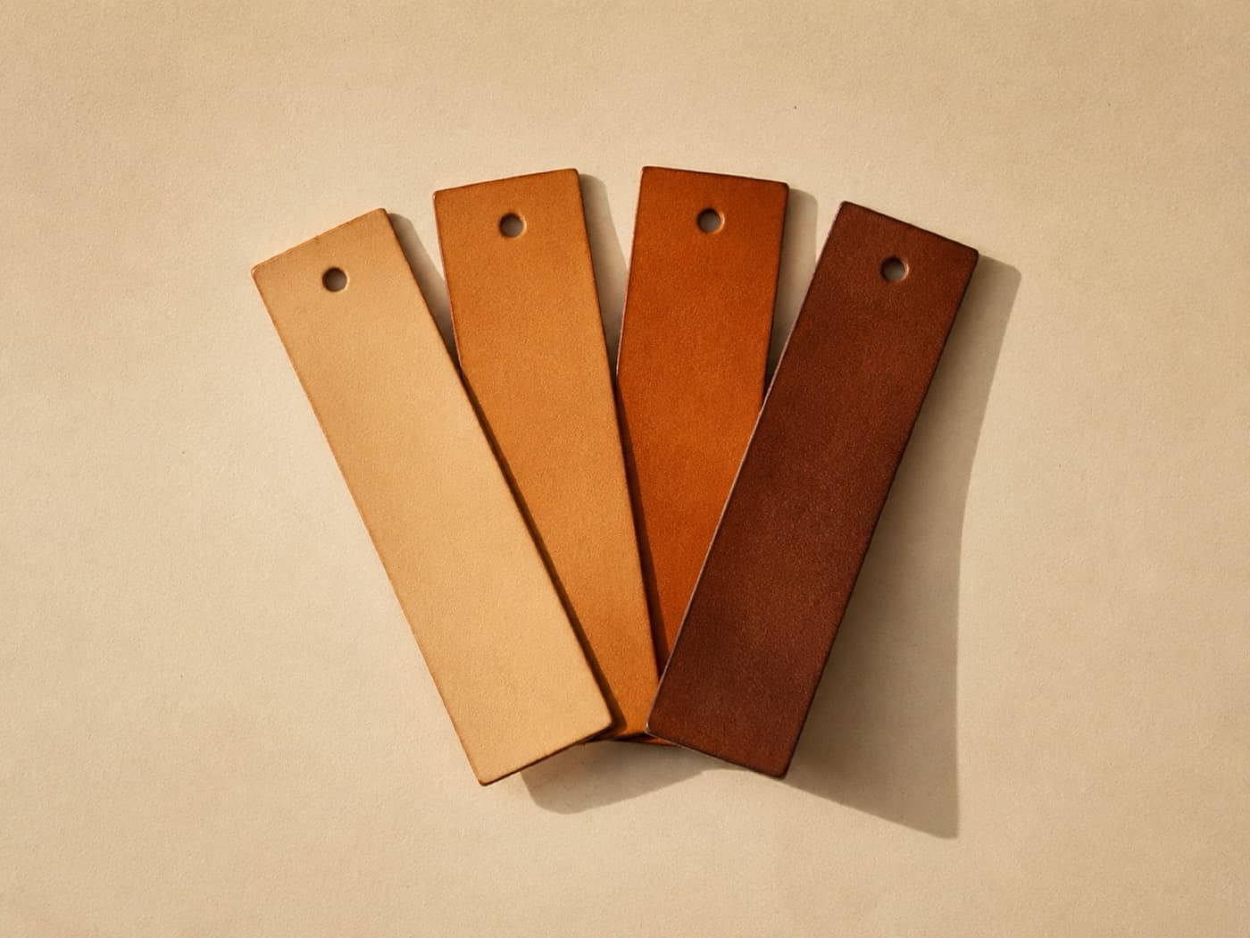 Four slim leather bookmarks in graduated tones, fanned out on cream paper