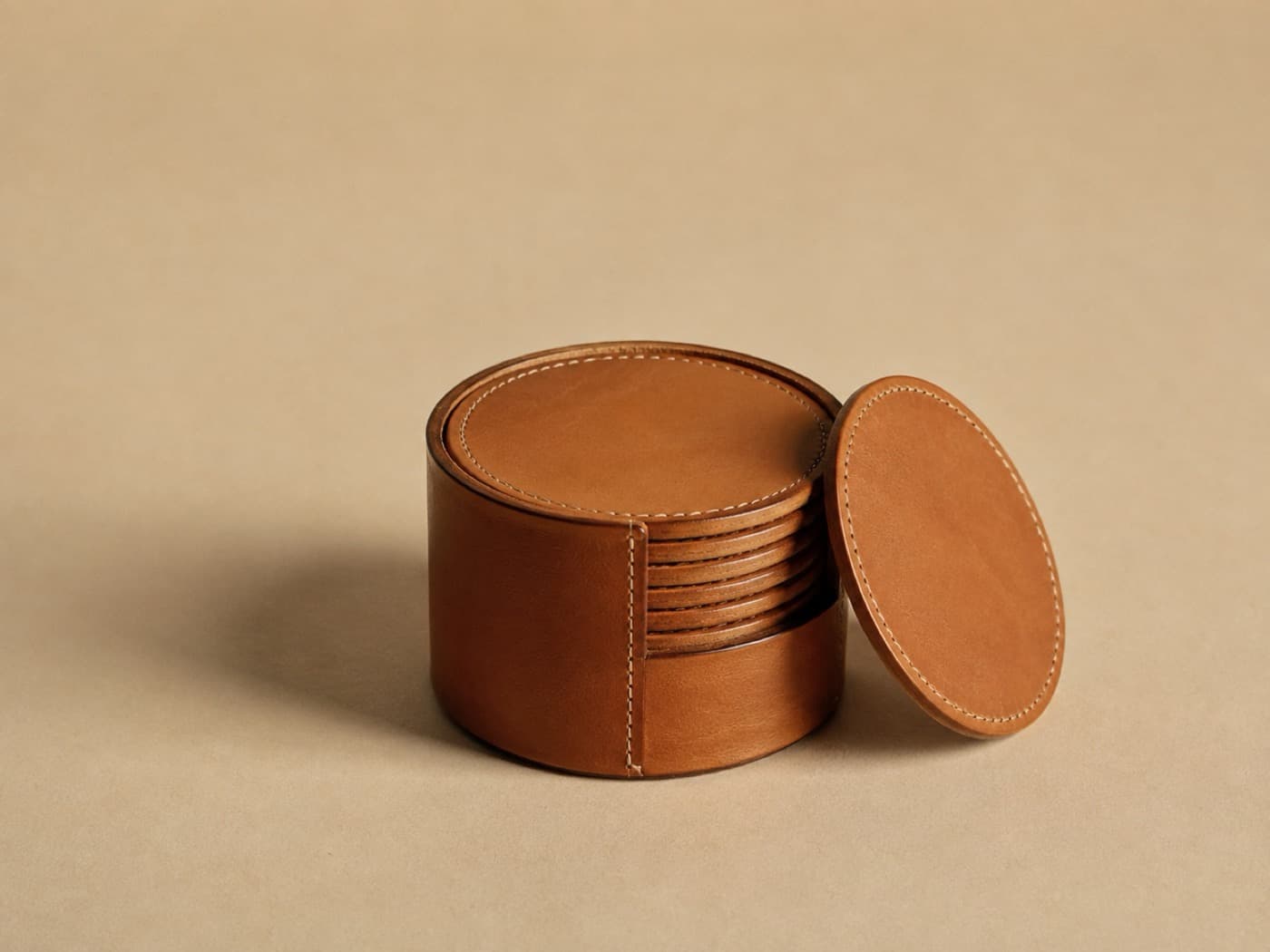 Six thick round leather coasters stacked in a stitched leather holder