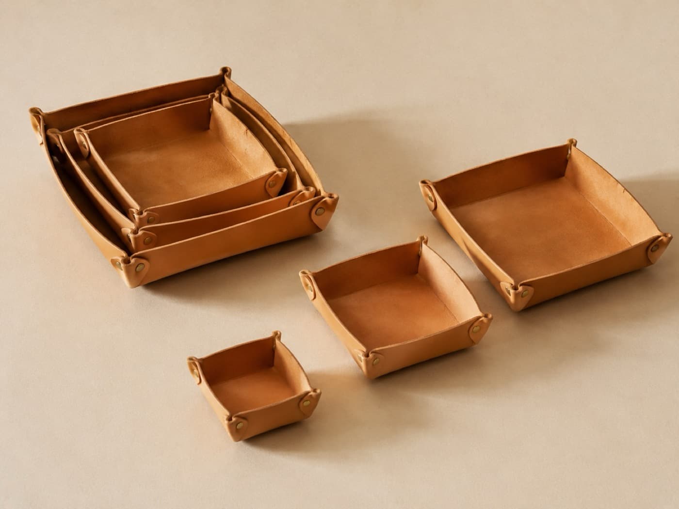 Three leather trays of graduated sizes, corners fastened with brass studs